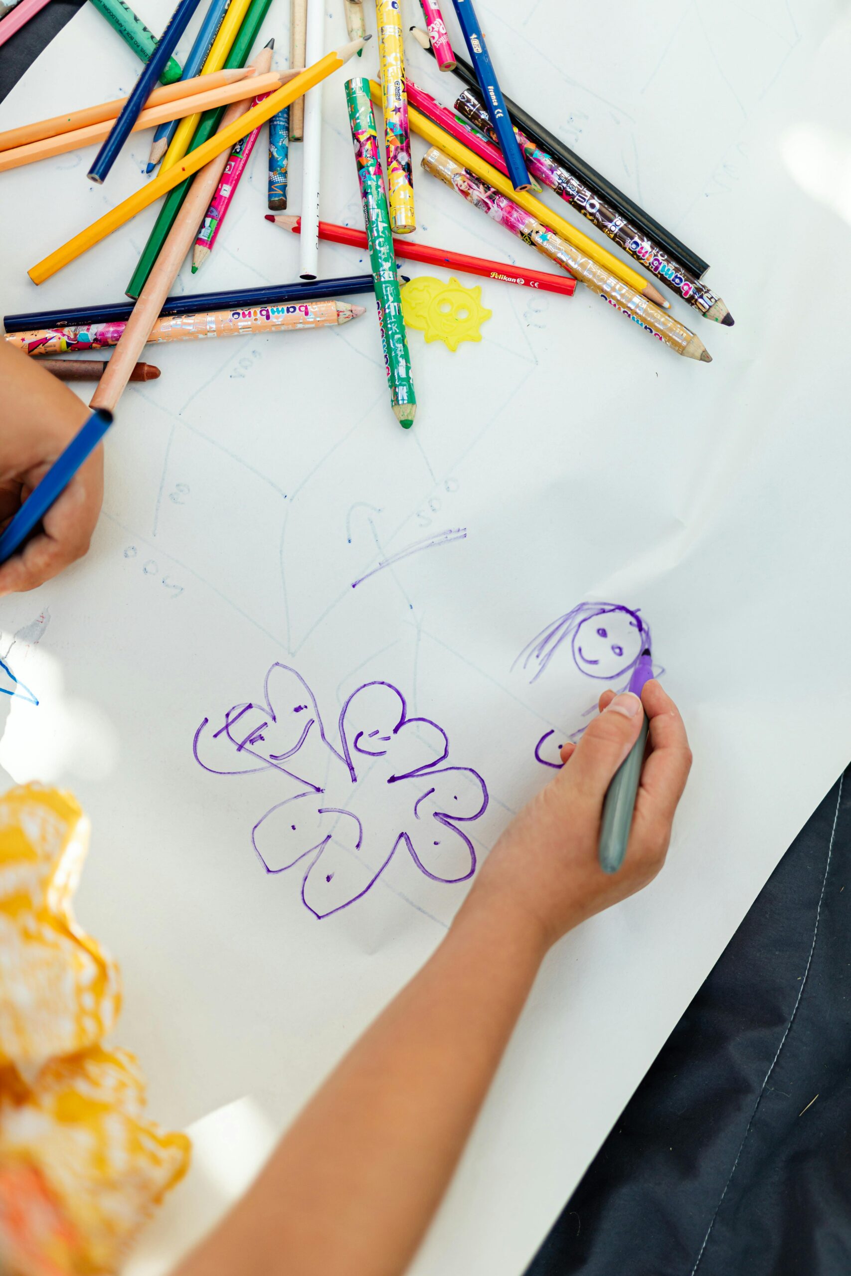 A child drawing on white paper with an assortment of colored pencils scattered around.
