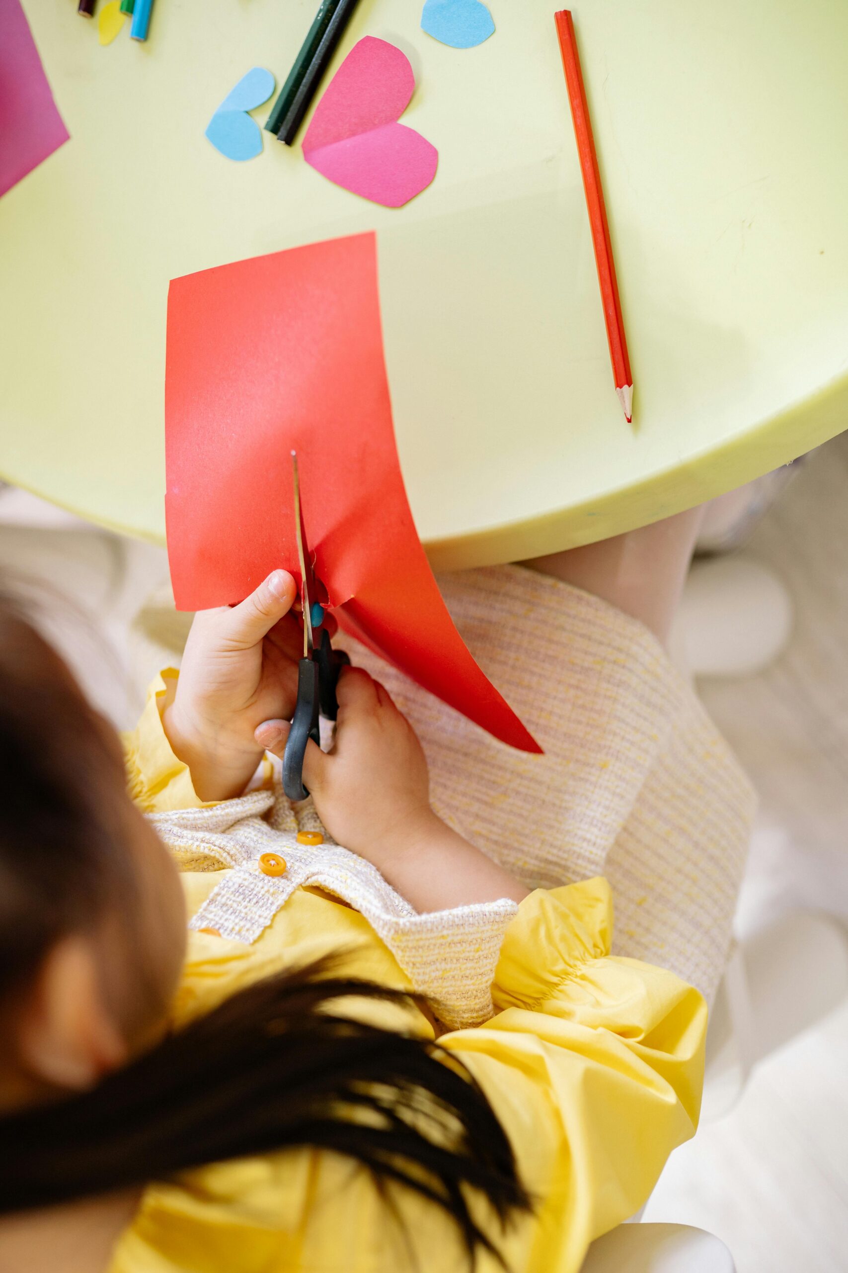 Top view of a girl cutting colored paper during a creative arts and crafts session indoors.